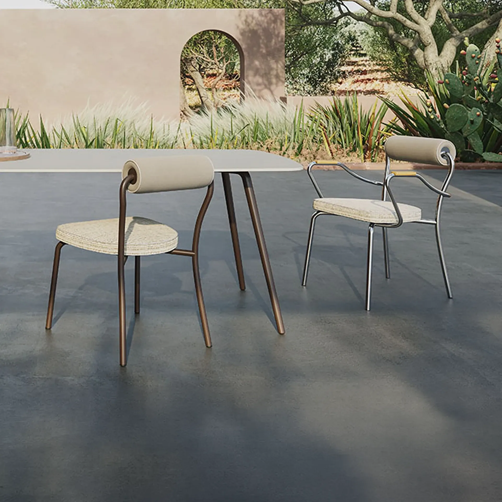 Two modern chairs, one bronze and one chrome, with beige upholstery, on a gray patio next to a table, with a garden and wall in the background.