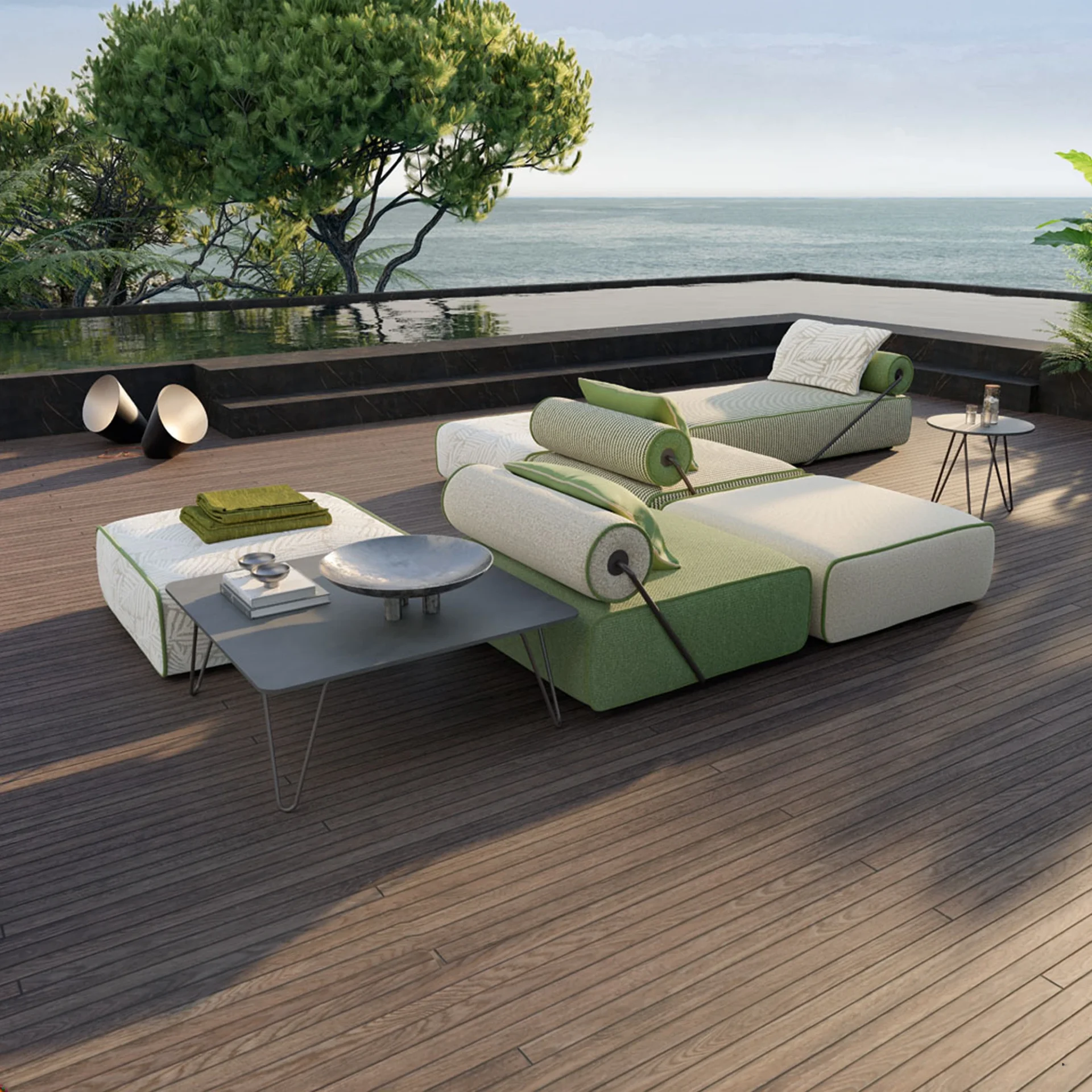 A luxurious outdoor modular sofa in green and off-white on a wooden deck, facing an infinity pool and the ocean, surrounded by lush trees.