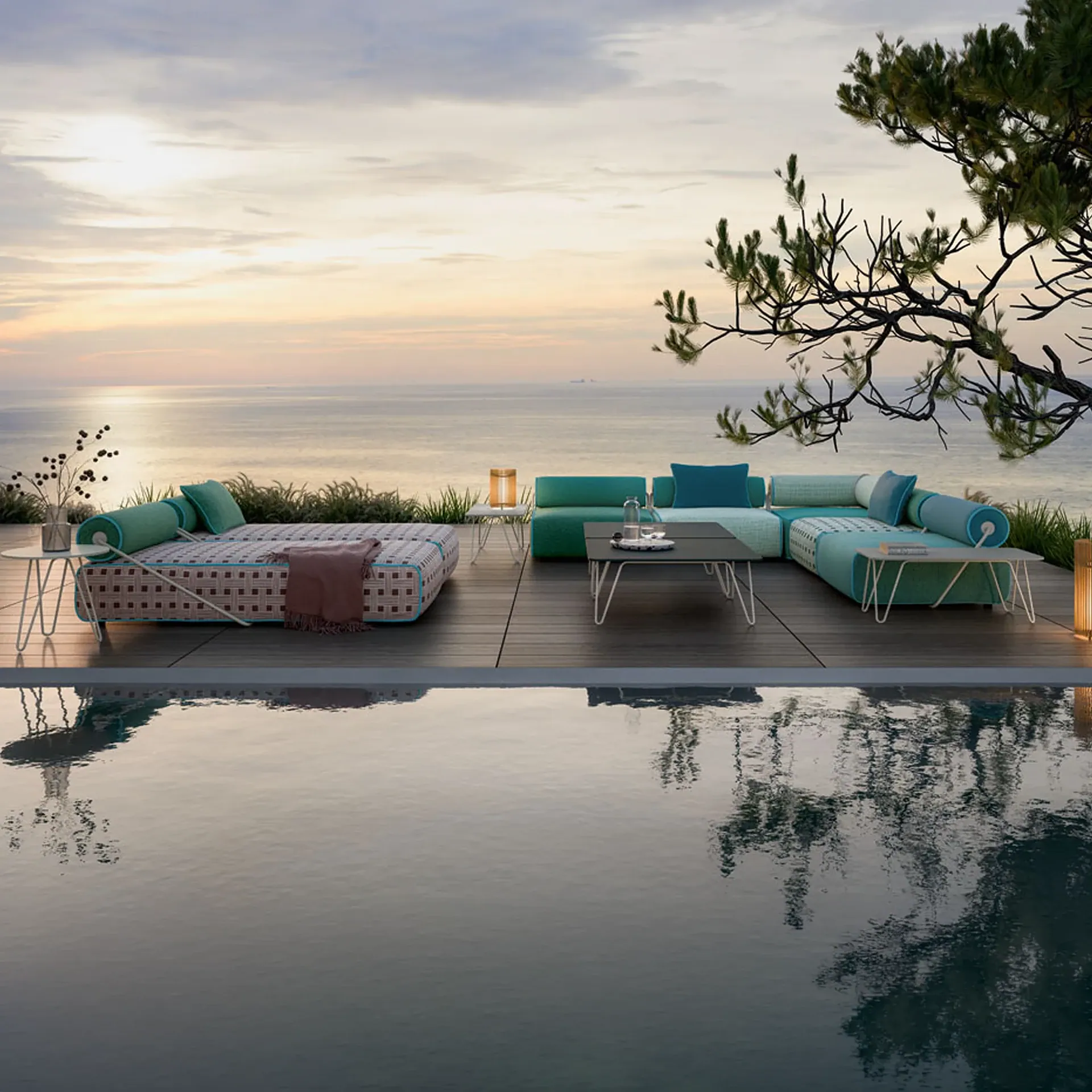 A luxurious outdoor patio with modular teal and beige furniture, overlooking a calm ocean at sunset, with a swimming pool reflecting the scene in the foreground.