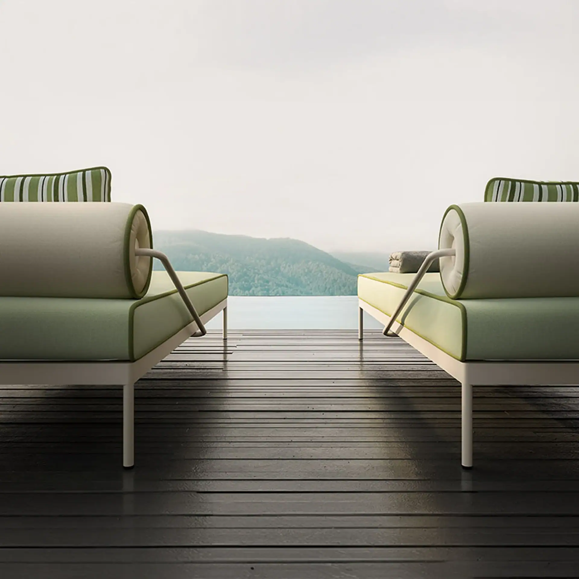 Two green and cream outdoor lounge chairs on a dark wooden deck, overlooking a lake and green mountains under an overcast sky.