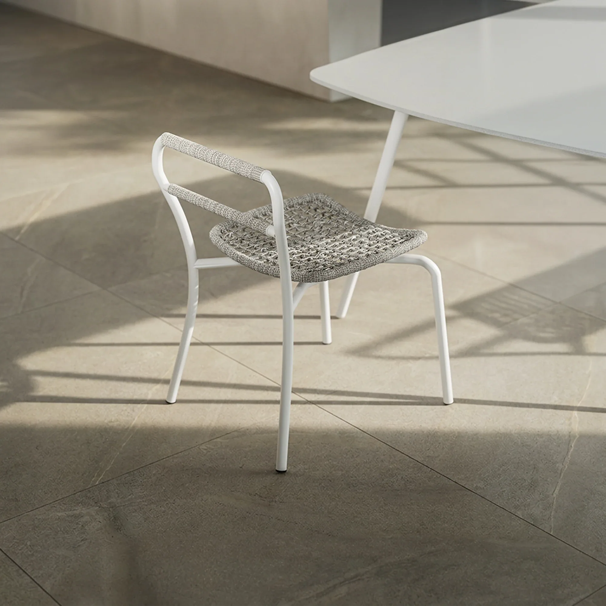 A white metal chair with a gray woven seat and back, next to a white table, on light-colored tiled flooring.