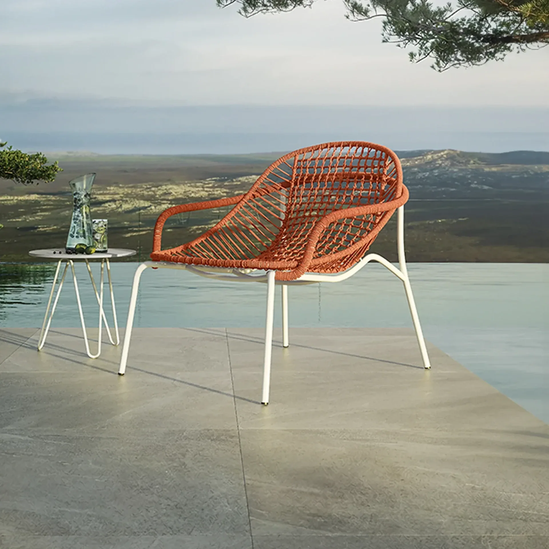 A modern orange woven outdoor chair and a small side table with a pitcher and glass on a grey tiled patio next to an infinity pool, overlooking a distant landscape under a cloudy sky.