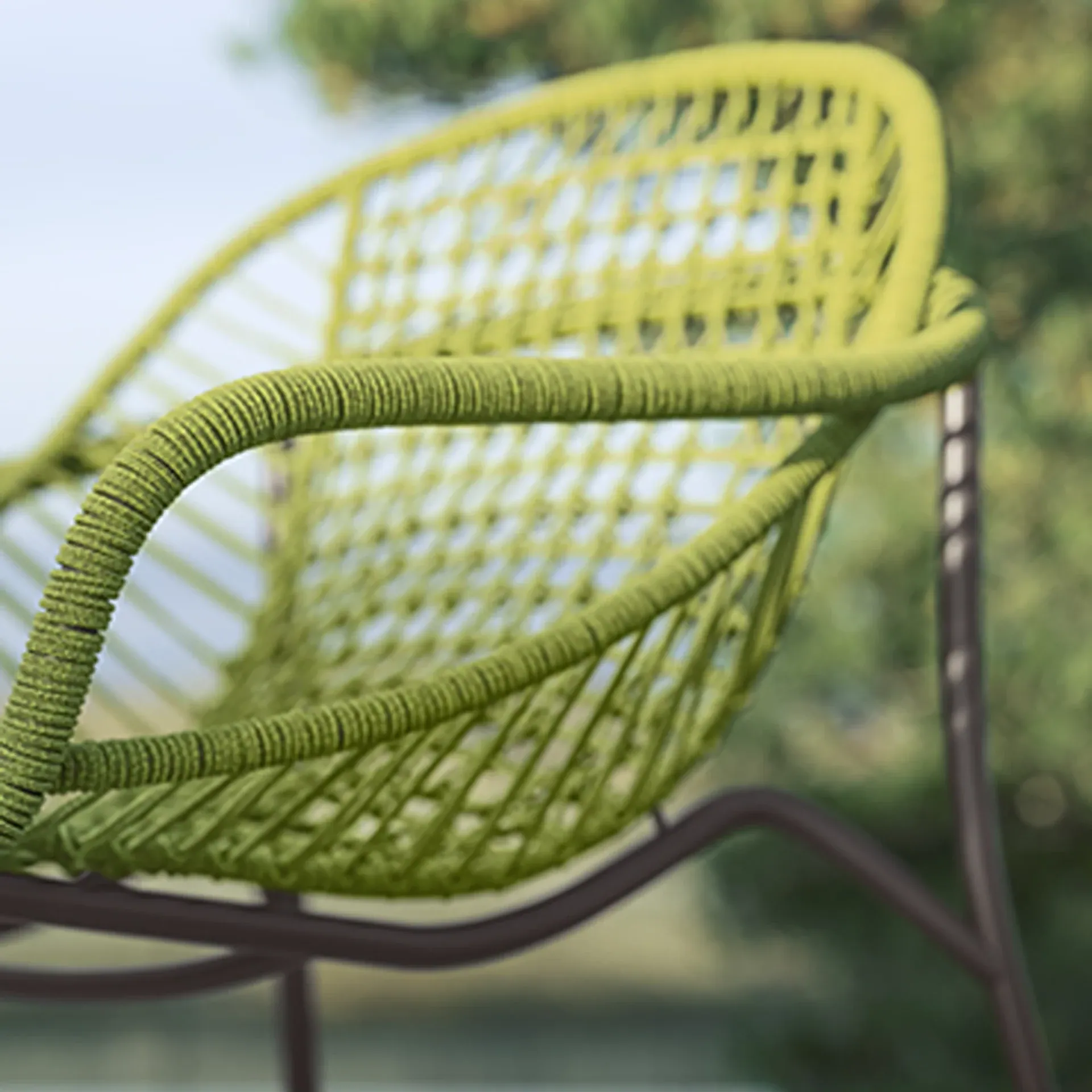 Close-up of a lime green woven outdoor chair with a dark frame against a blurred green and blue background.