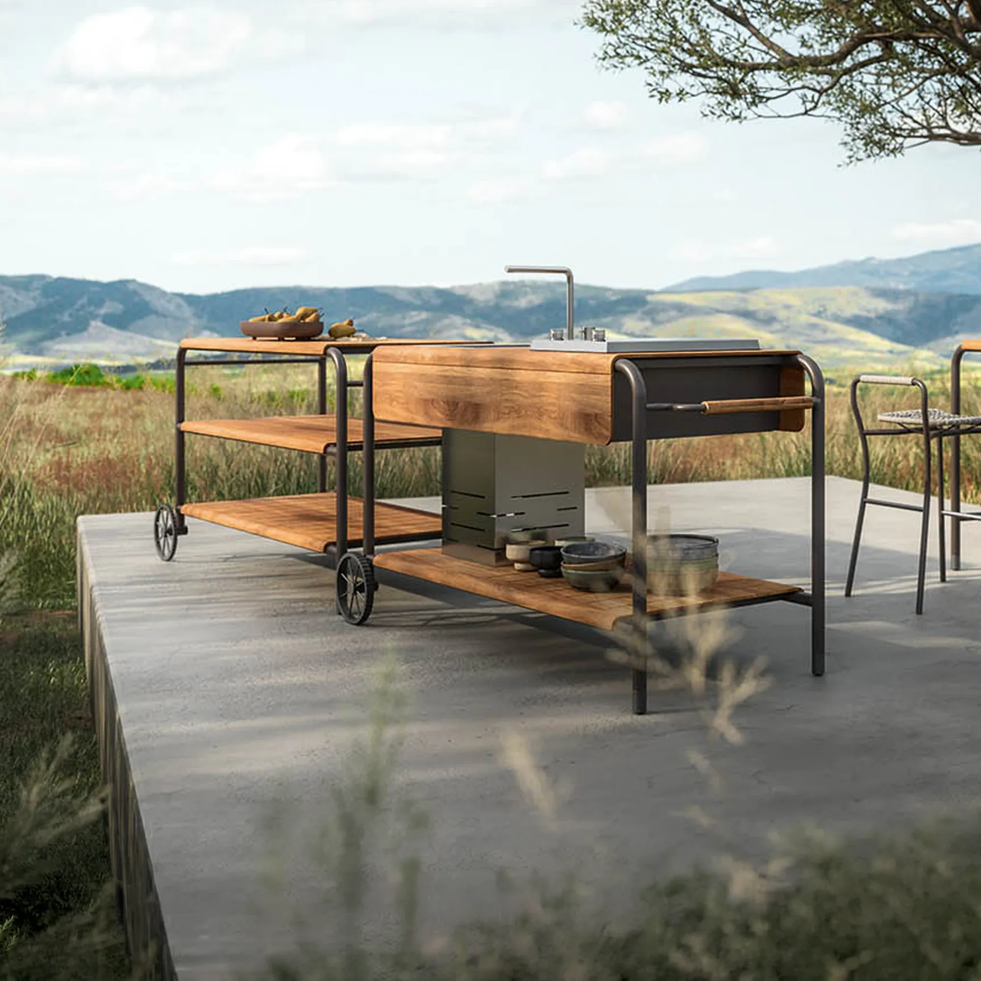 A modern outdoor kitchen cart with a sink, grill, and wooden shelves on a concrete patio overlooking a mountainous landscape.