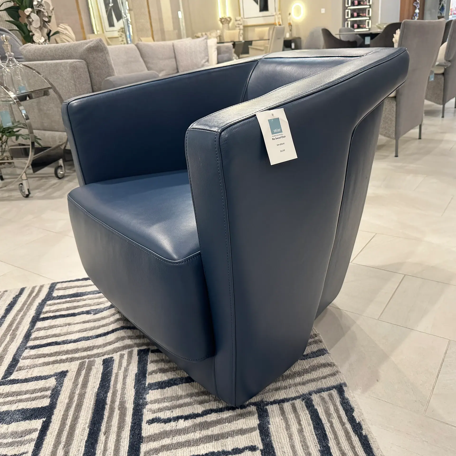 A dark blue leather swivel armchair with a price tag on a striped rug in a furniture showroom.