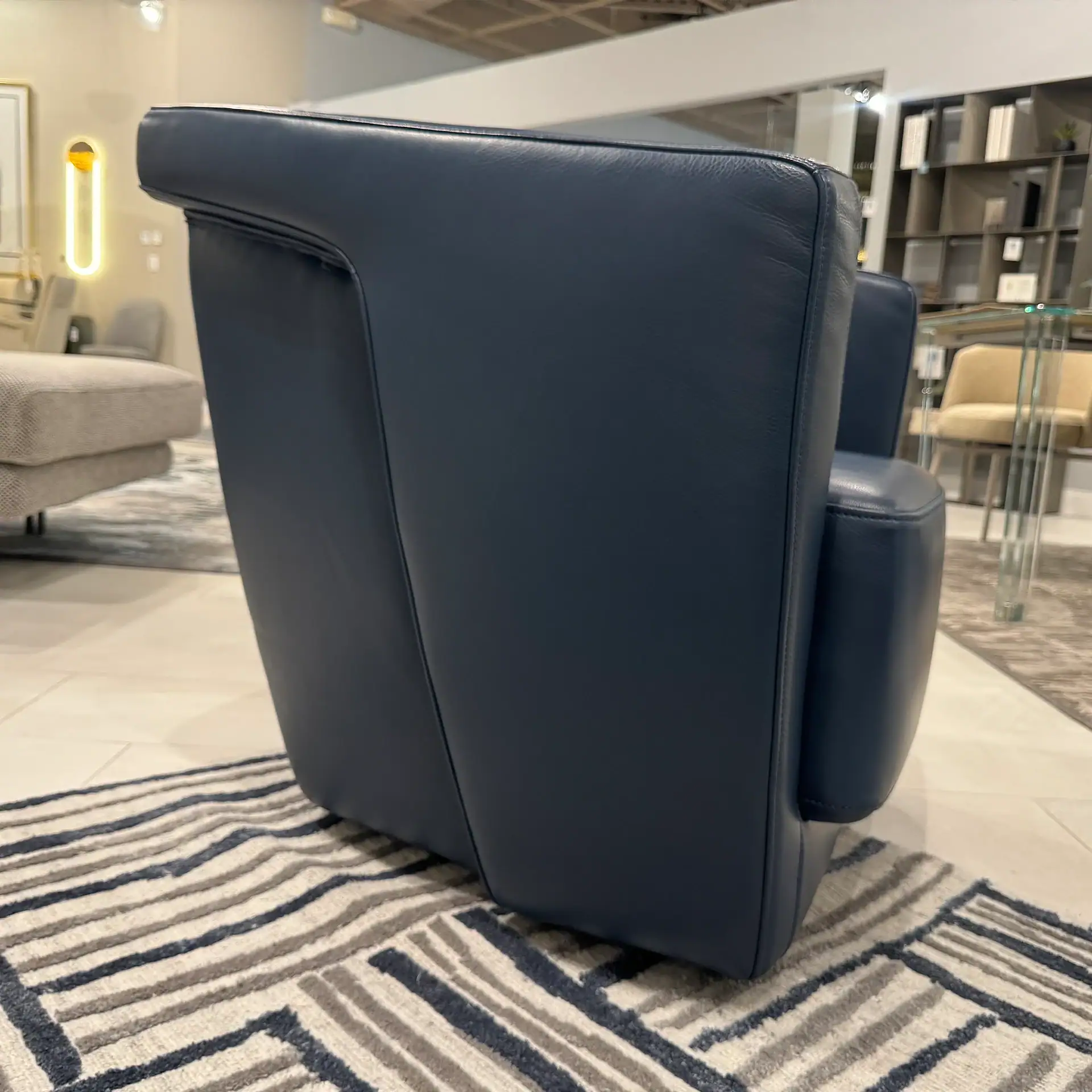 A dark blue leather armchair sits on a striped and geometric patterned rug in a modern room.