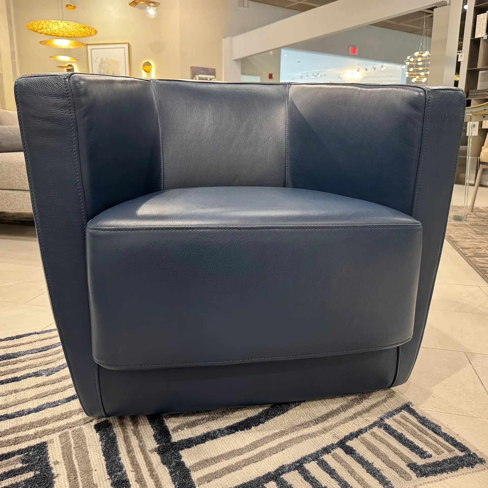 A dark blue leather armchair with a modern design sits on a patterned rug in a furniture showroom.