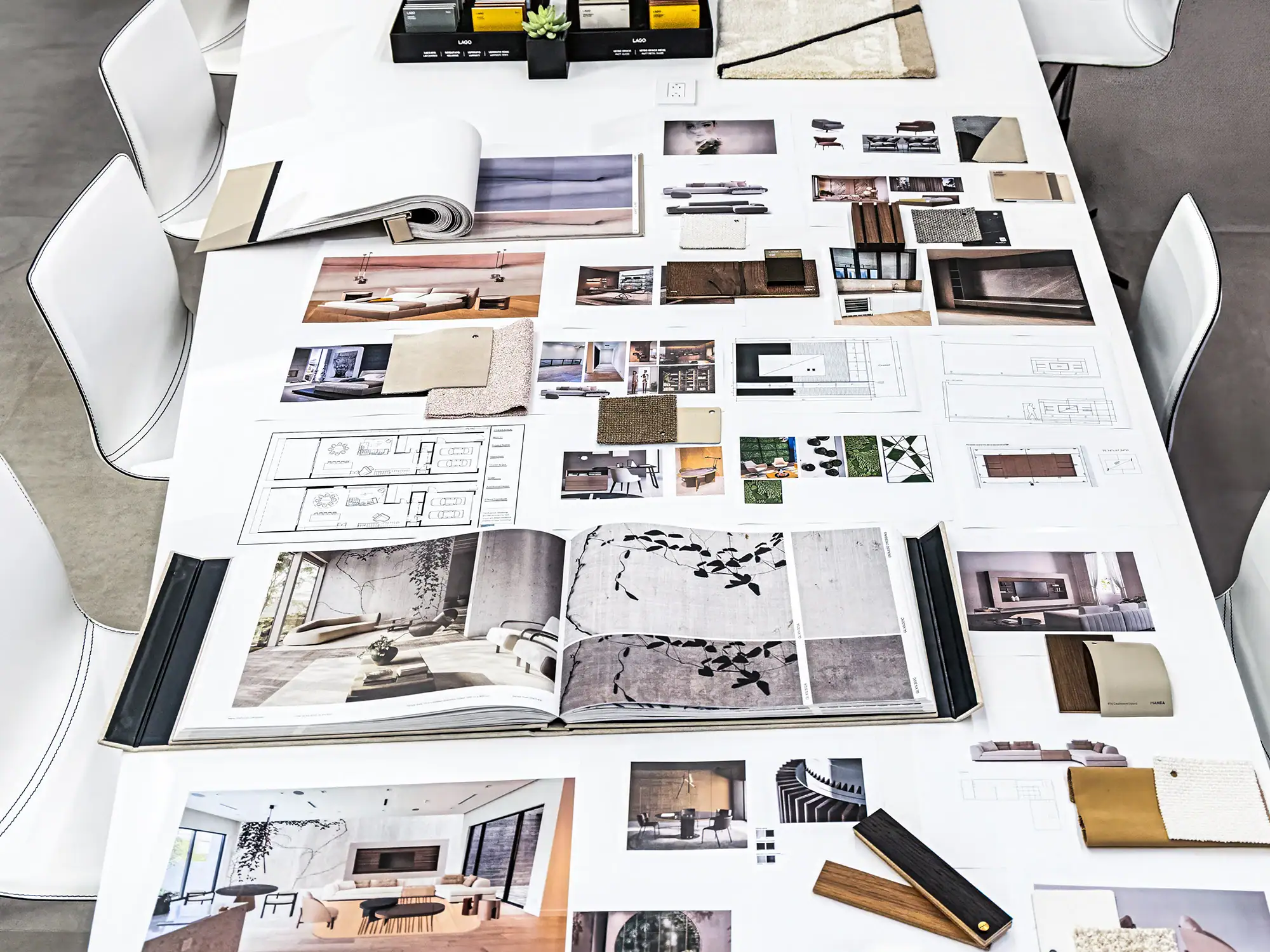 Overhead view of a white table covered with interior design plans, photos, and material samples, surrounded by white chairs.